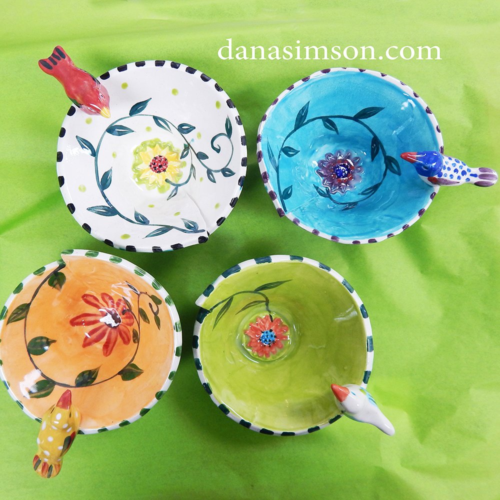 A set of four different colored Bird Bowls looking down to see the daisy and vine design painted on each interior.